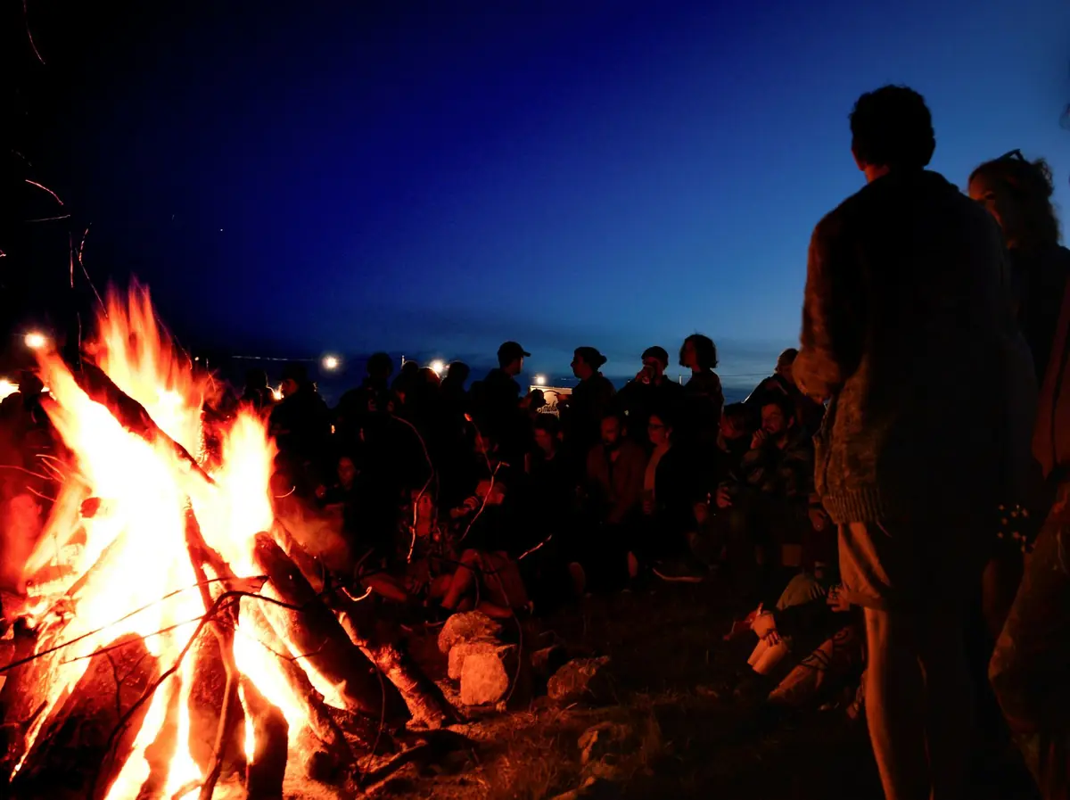 A group of people gathered around a large bonfire at dusk